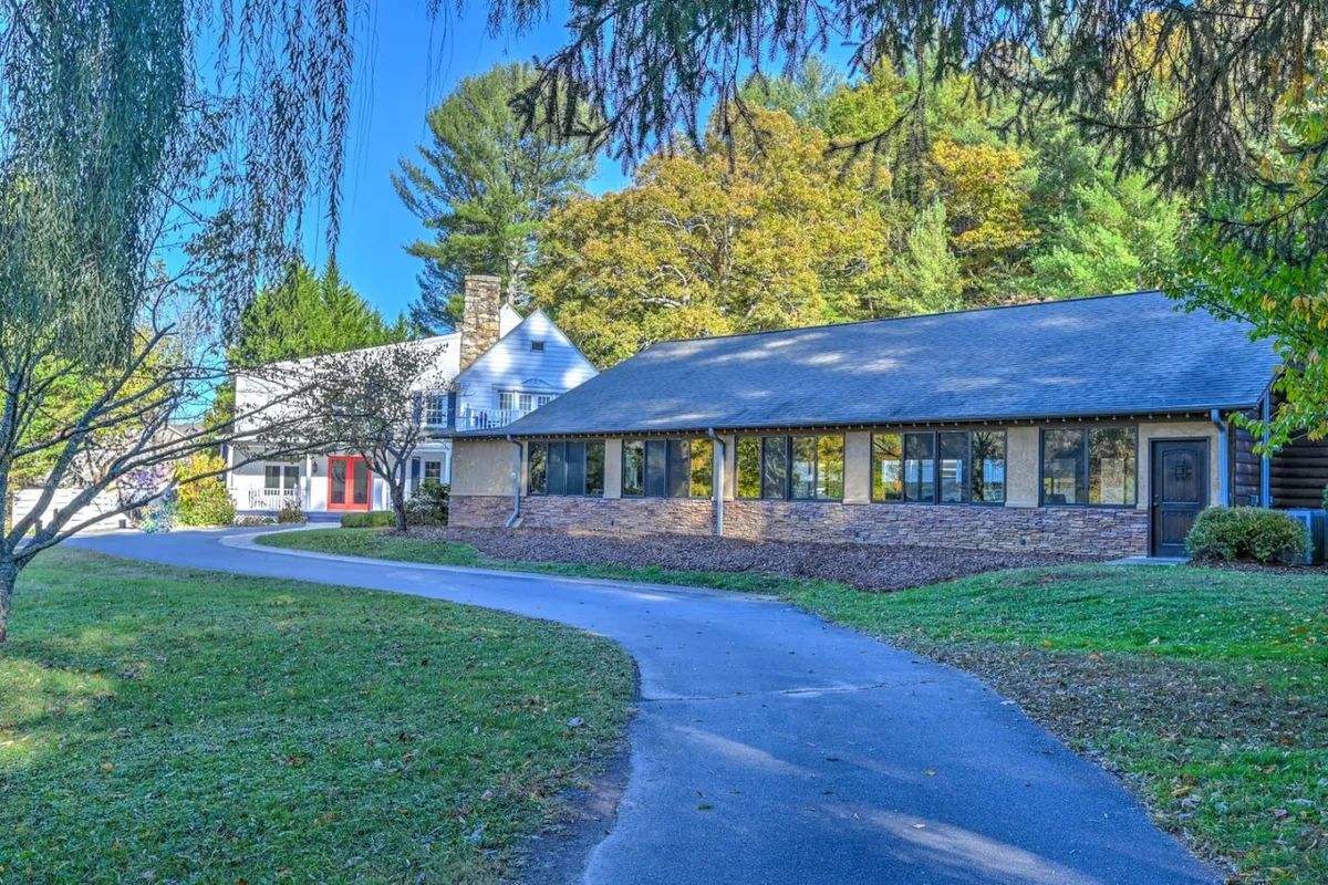 This exterior image shows the main building of Willow Ridge, surrounded by mature trees. The inviting pathway leads up to a broad porch, with enough space for guests to gather and enjoy the outdoors. The scene is bathed in golden evening light, suggesting a welcoming spot for group activities or winding down after a day out.