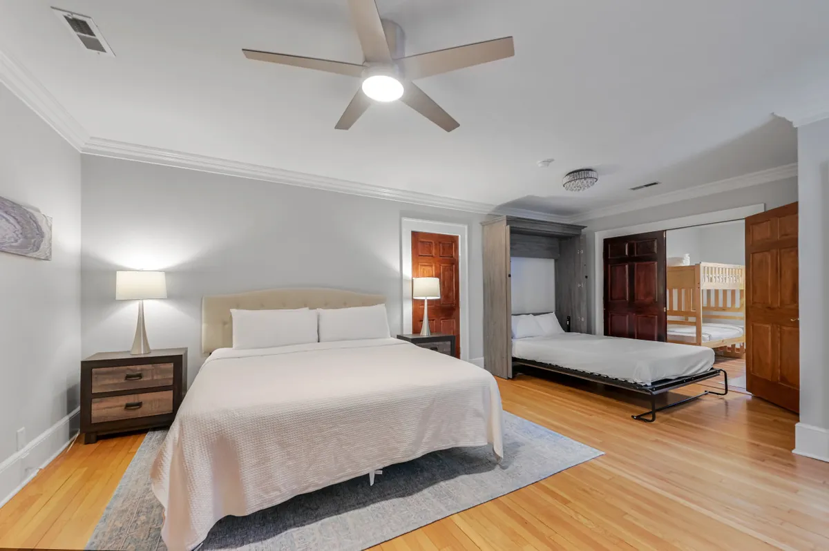 A peaceful bedroom featuring a king-sized bed as the centerpiece, complemented by a foldable bed tucked nearby. Wooden doors and soft lighting create a calm, welcoming atmosphere ideal for rest and family time.