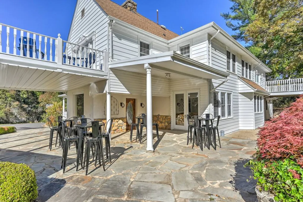 The photo highlights a cheerful outdoor patio with a stone pathway, comfortable seating, and the house in the backdrop. The area is naturally lit and framed by greenery, creating an ideal spot for evening games, conversations, or celebratory toasts beneath the open sky.