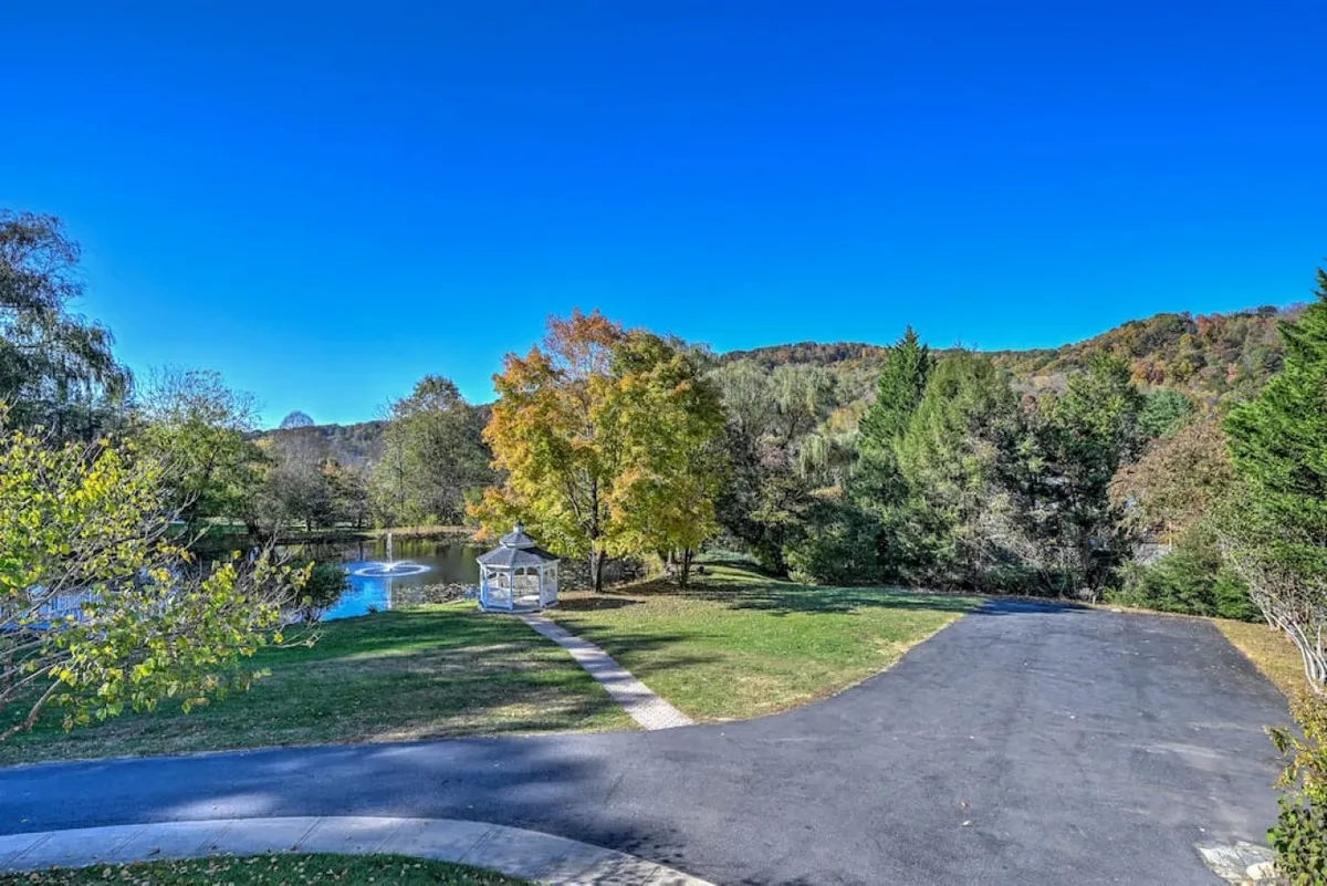 A tranquil scene featuring a peaceful gazebo nestled among colorful trees, with reflective water in the foreground. The landscape showcases vibrant foliage, suggesting the allure of autumn and the beauty of changing seasons.
