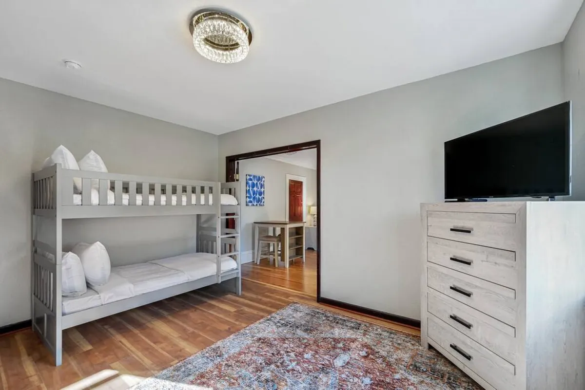 A comfortable bedroom with a bunk bed, television, dresser, and area rug. The space is designed to be both functional and inviting, suitable for relaxing, playing games, or catching up on sleep after a busy day.