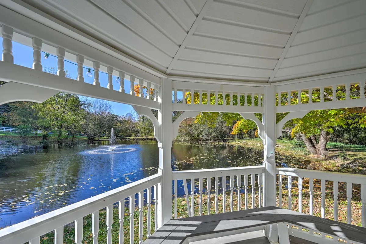 The image showcases a tranquil outdoor scene featuring a picturesque gazebo overlooking a serene pond with a fountain, surrounded by vibrant autumn trees. The setting invites relaxation, quiet gatherings, and enjoying the natural beauty of Swannanoa, North Carolina.