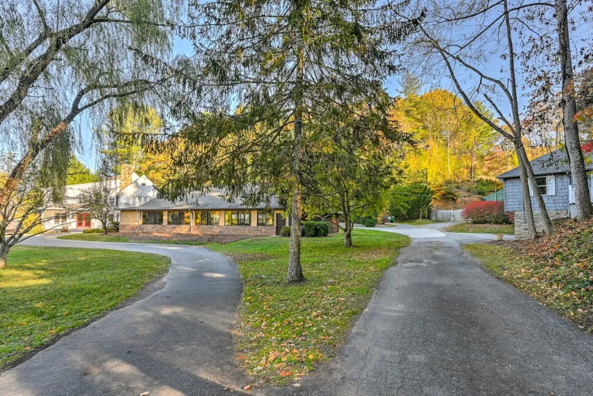 This exterior image showcases the main house set amid mature trees and thoughtful landscaping, with a wide driveway gently curving toward the entrance. The space feels tranquil and expansive, ideal for gathering guests and hosting memorable outdoor events.